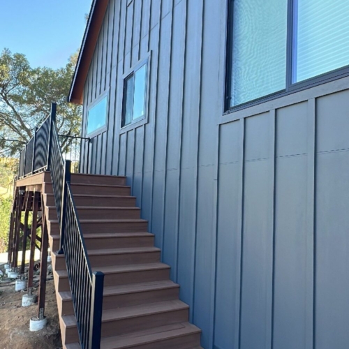 grey house with wood stairs and a black railing